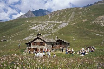 L'extérieur du refuge PNV de Vallonbrun avec de nombreux randonneurs. Prairie de fauche à renouée bistorte au premier plan.